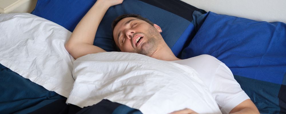 Homem deitado de boca aberta e tendo problemas para dormir